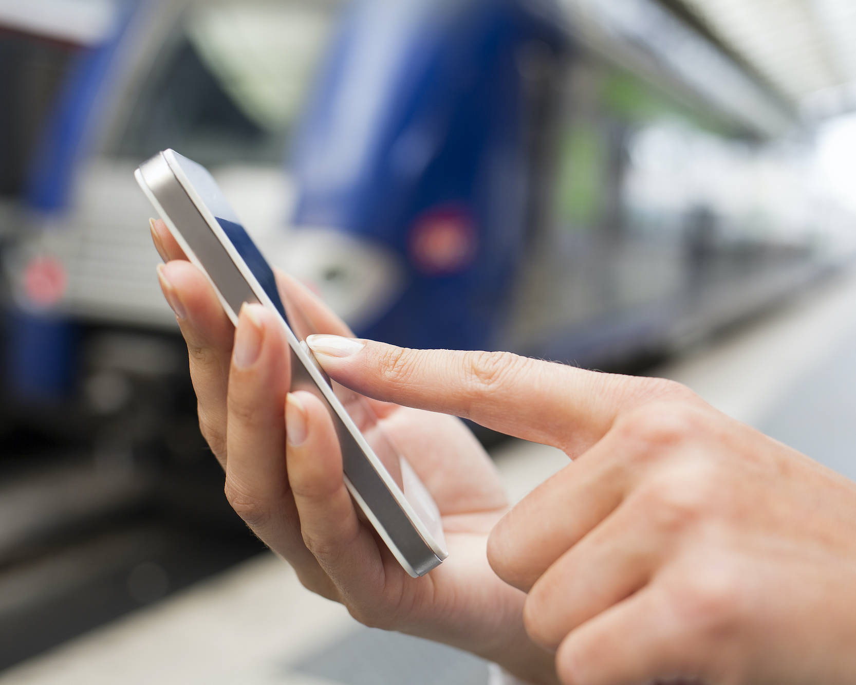 Frau bedient ihr Smartphone am Bahngleis