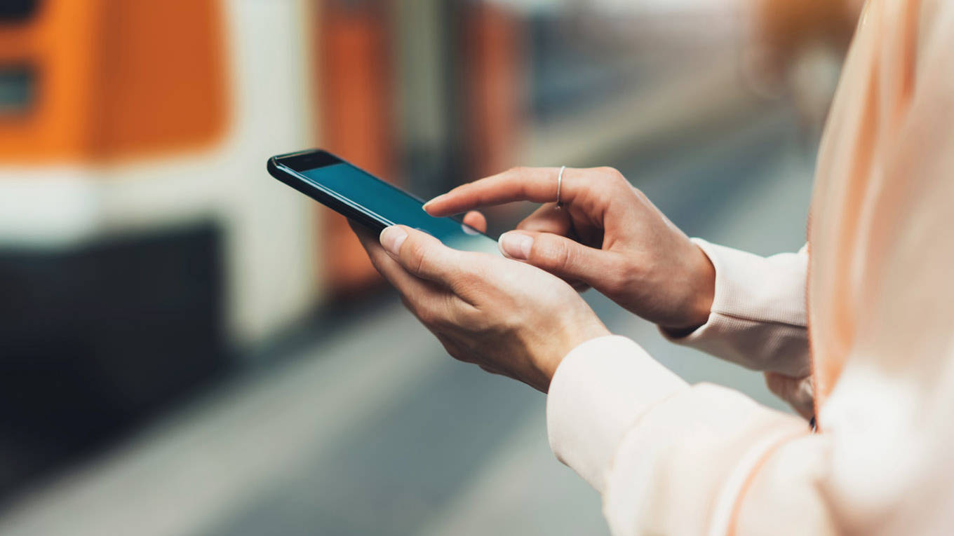 Frau steht mit ihrem Smartphone vor der Bahn.